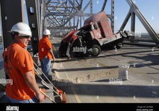 Two men in orange shirts and hard hats standing next to a truck.